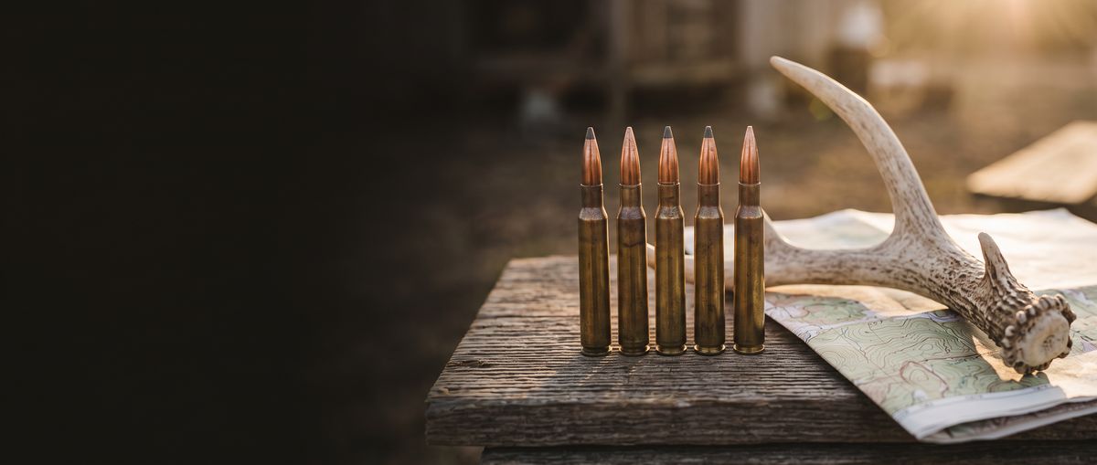Five rifle cartridges standing beside a deer antler on a map