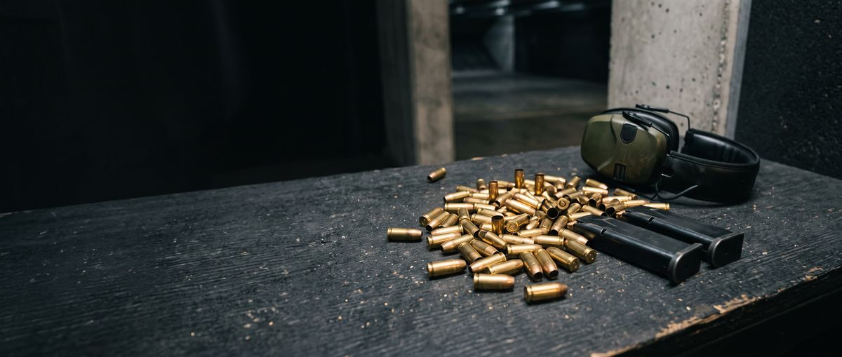 Spent brass, pistol magazines and ear protection on a range bench