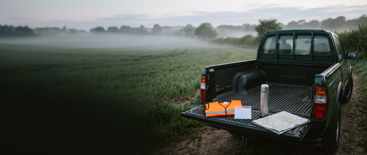 Pickup tailgate with a blaze orange vest, map and thermos at a misty field edge