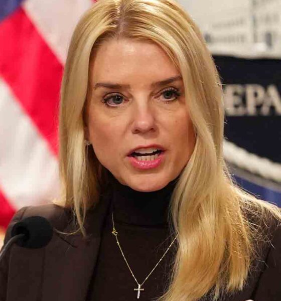 Pam Bondi speaking at DOJ podium in 2025, amid gun registry controversy - official portrait with American flag background