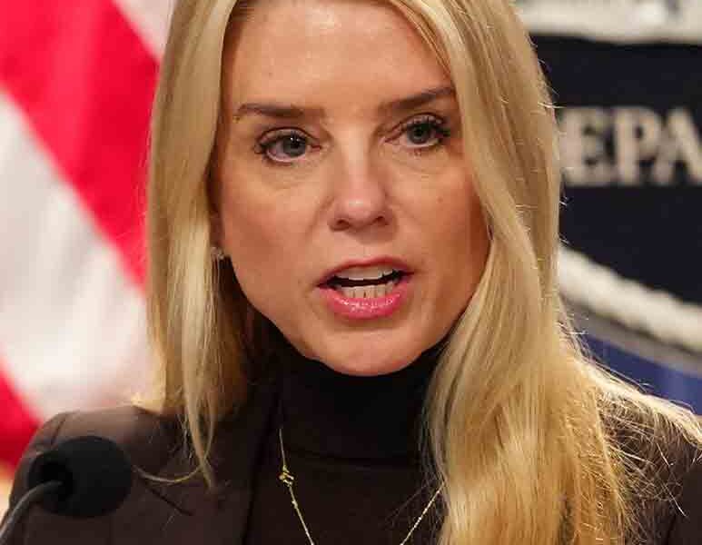 Pam Bondi speaking at DOJ podium in 2025, amid gun registry controversy - official portrait with American flag background