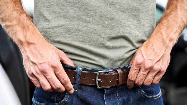 Concealed carry gun in waistband - Freedom’s Lodge Close-up of a person adjusting a brown leather belt at the waist over blue jeans and a gray shirt on.
