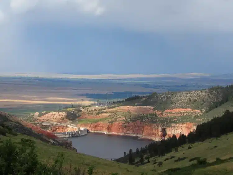 bighorncanyonjpg - Freedom’s Lodge A dammed lake set in a canyon with red cliff walls and green hills, under a cloudy sky in the distance.