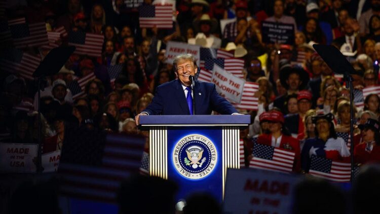 trump-midterm-convention-1 - Freedom’s Lodge Speaker at a podium with the U.S. presidential seal addressing a large crowd at a political rally with American flags nearby.